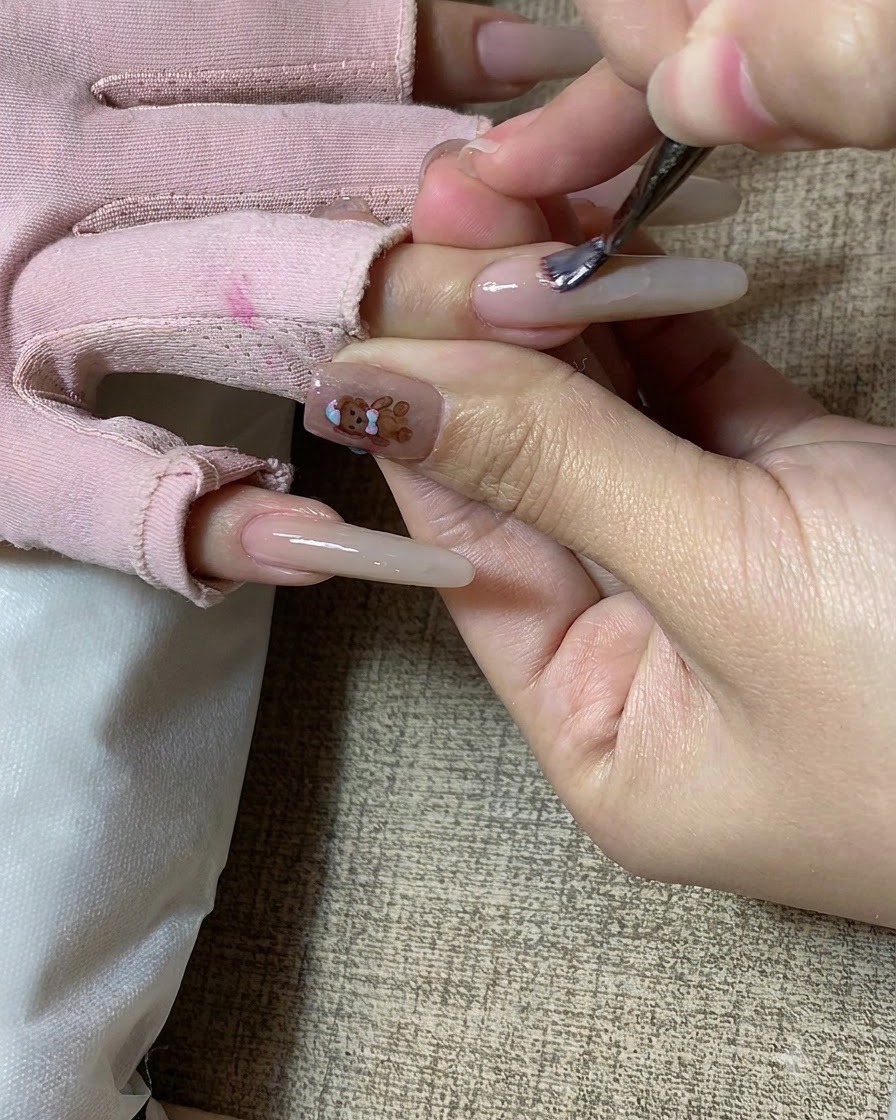 Un pincel de uñas aplicando gel de color té con leche sobre una uña esculpida larga.