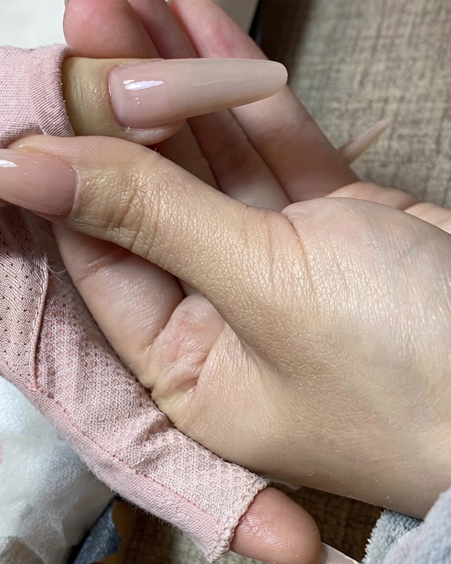 Una vista en primer plano de una mano sosteniendo una uña esculpida con manicura de té con leche terminada.