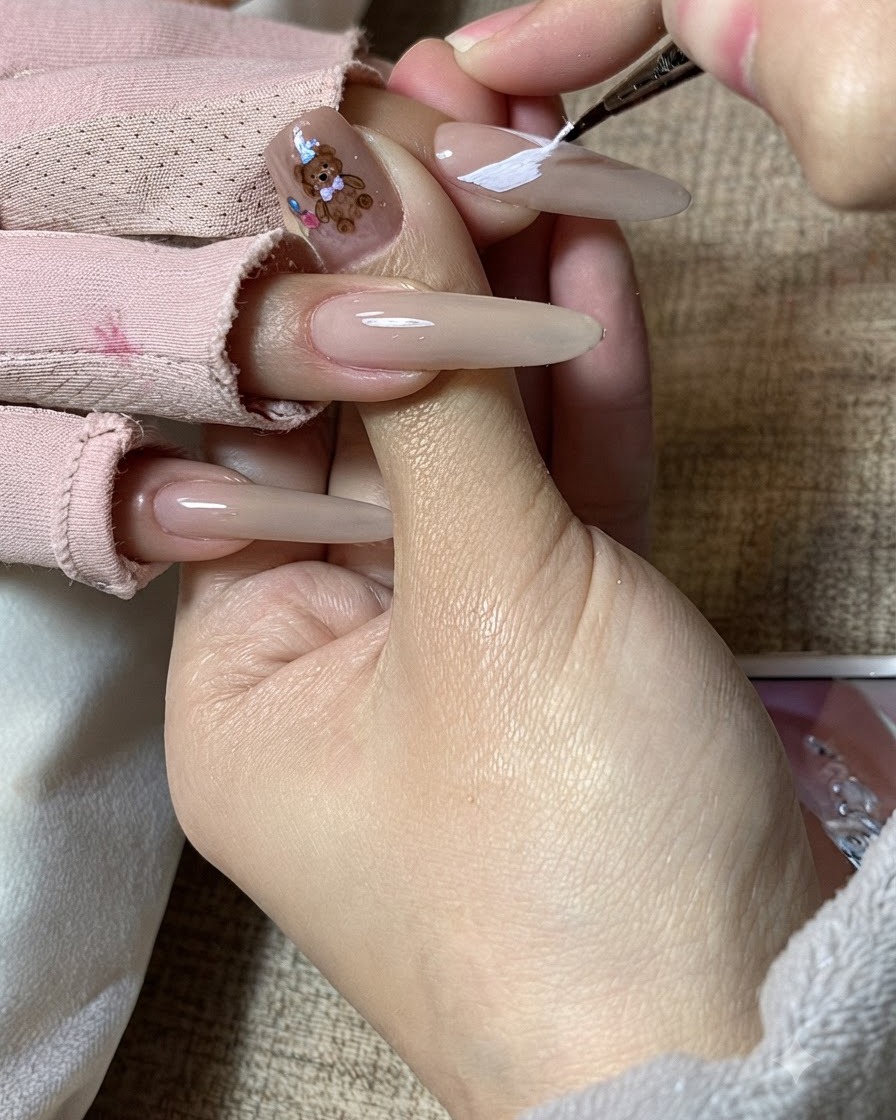 La mano de una artista de uñas refinando patrones de alas de mariposa blancas en una uña alargada.
