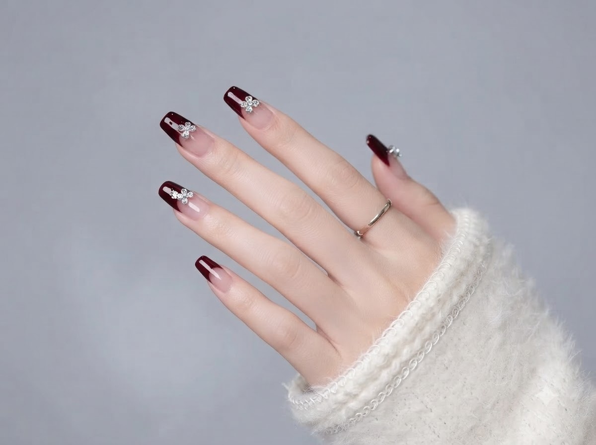 Una mano mostrando la disposición completa de las uñas de gel en tonos nude y burdeos con detalles de cristal.