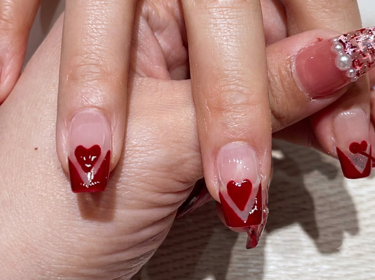 Una vista en primer plano de una mano que muestra los dedos con manicura francesa en V roja y corazones rojos centrados.