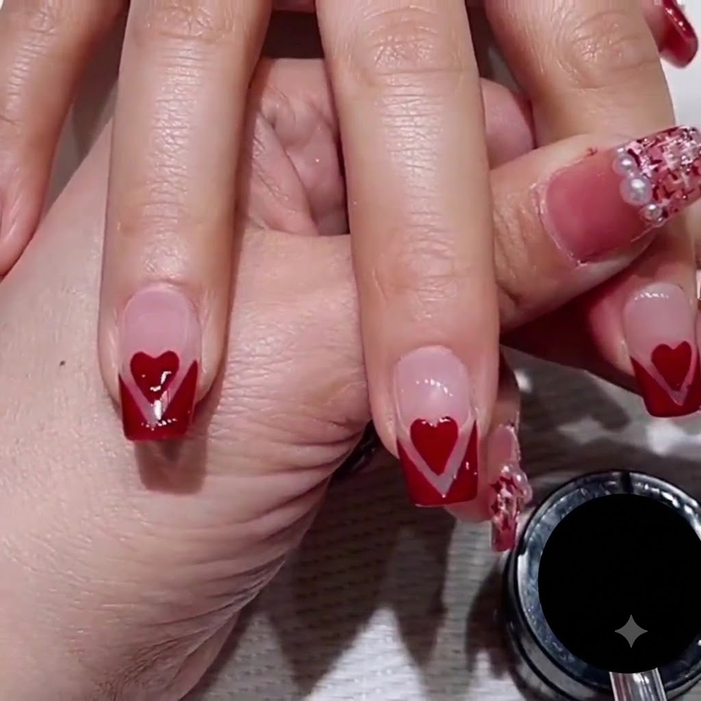 Un primer plano de la mano de un artista de uñas utilizando un pincel estriador delgado para trazar una fina línea de purpurina oro rosa a lo largo del borde de un diseño de uña con punta en V roja.