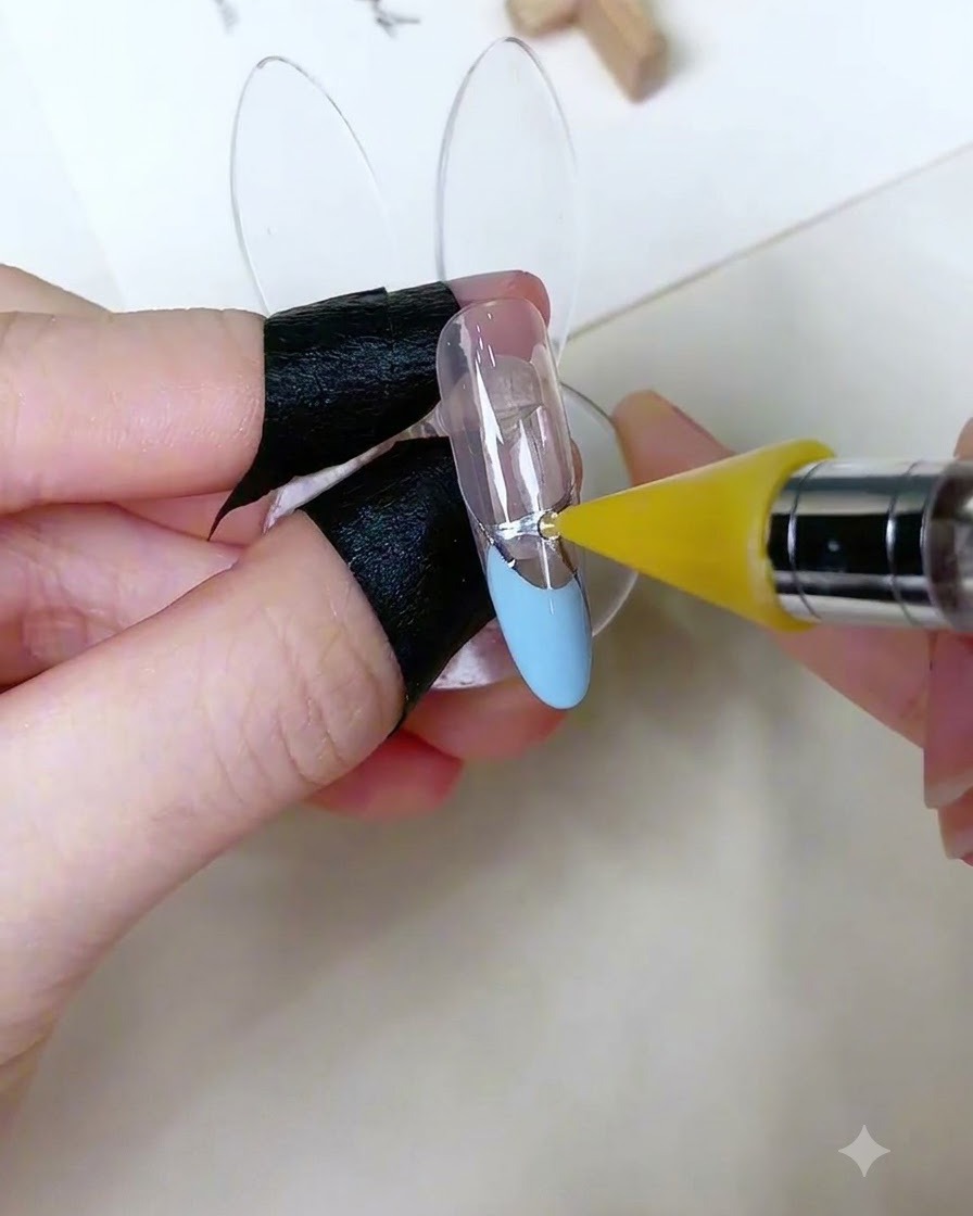 Una herramienta de recogida especializada colocando un pequeño diamante de imitación redondo sobre un punto de gel adhesivo en una uña decorada.