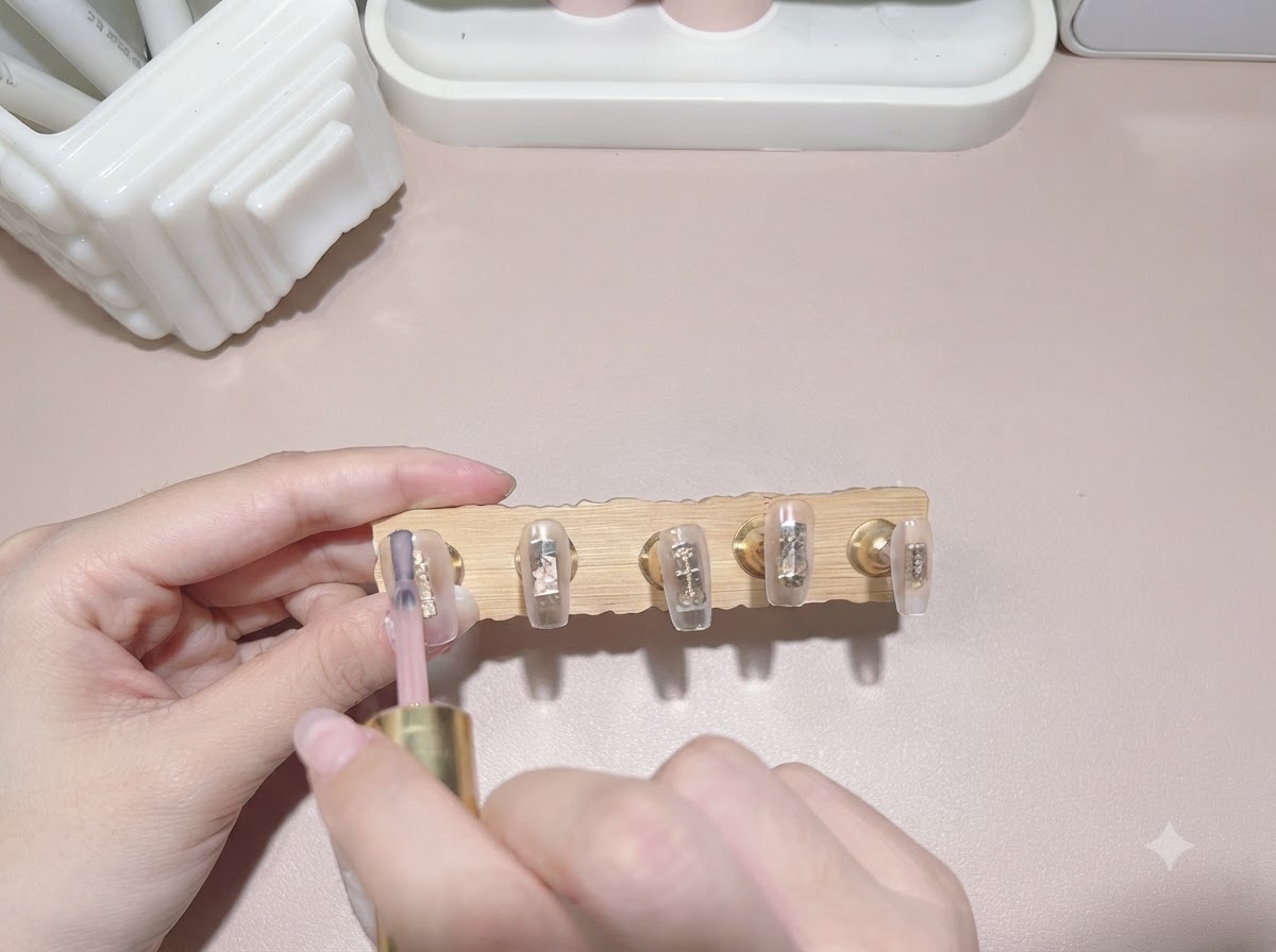 Un pincel aplicando esmalte en gel de color té con leche traslúcido sobre la punta de una uña.