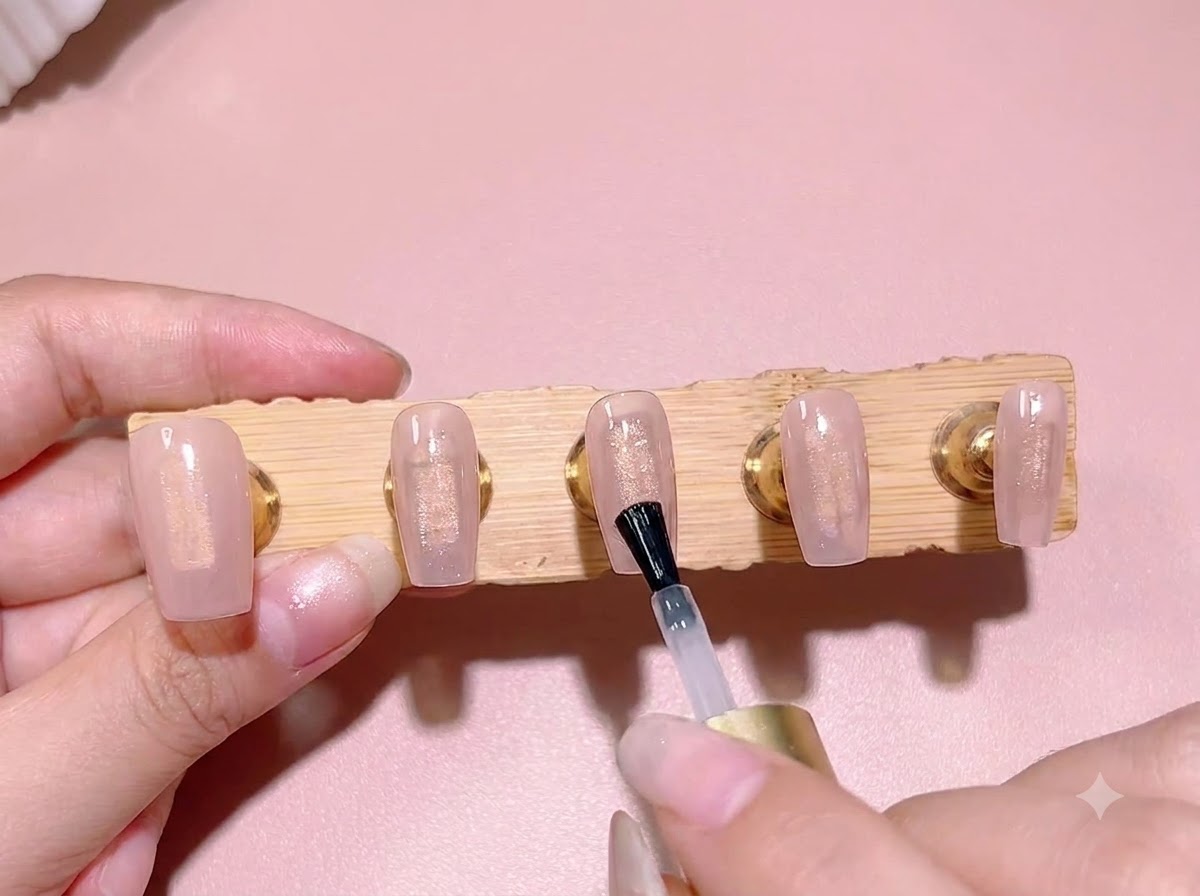 Un pincel de esmalte estándar aplicando una capa de gel de expansión transparente sobre un color base rosa traslúcido en la punta de una uña.