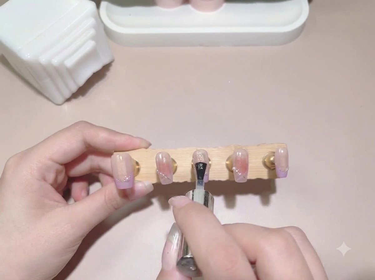 Un pincel de capa superior aplicándose a través de un soporte de exhibición de uñas postizas pintadas terminadas.