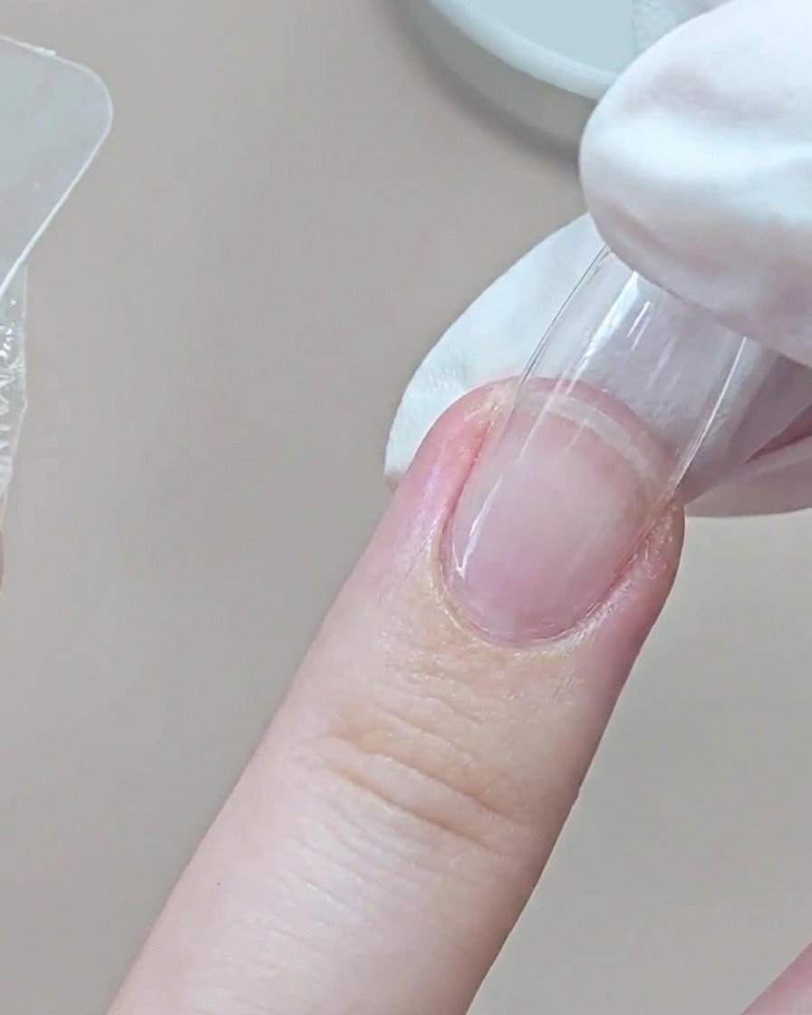 Un dedo con guante presionando un molde dual transparente sobre el dedo anular cerca de la zona de la cutícula.