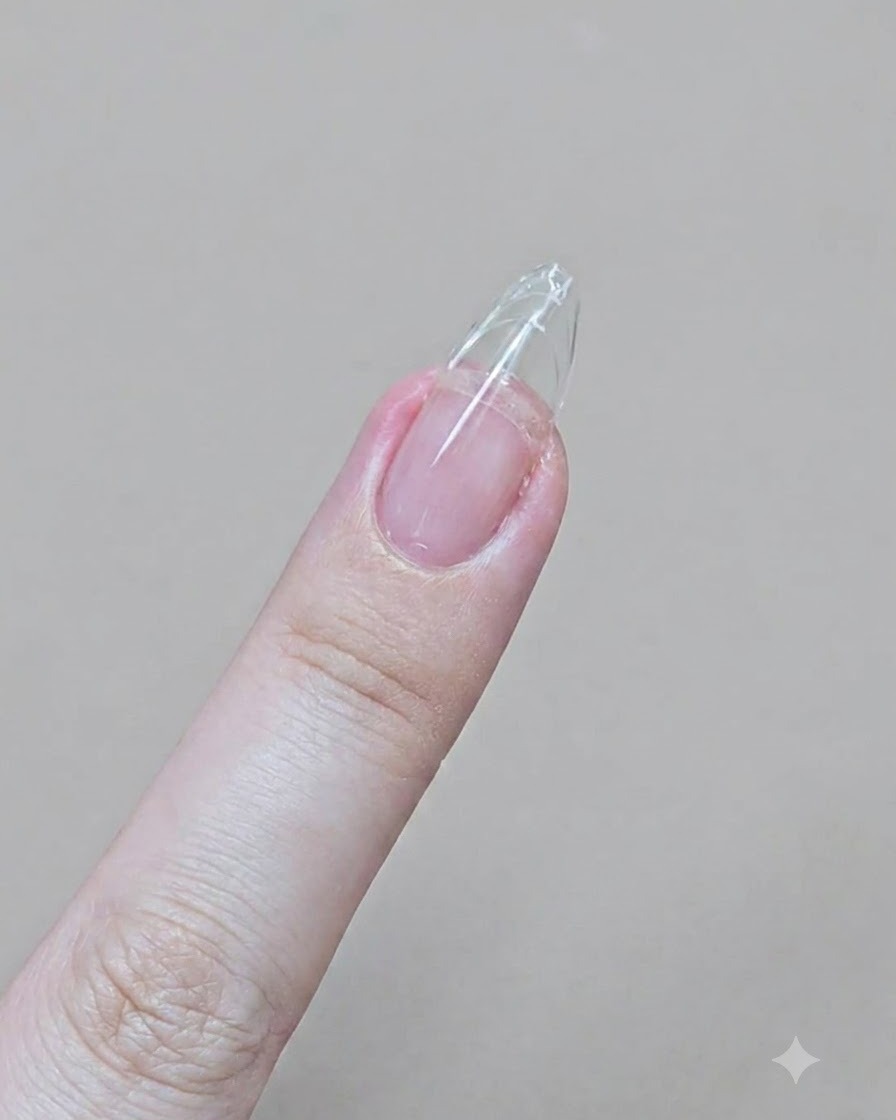 Un dedo con una extensión de gel transparente siendo limado en una punta de almendra afilada con una lima de cartón.