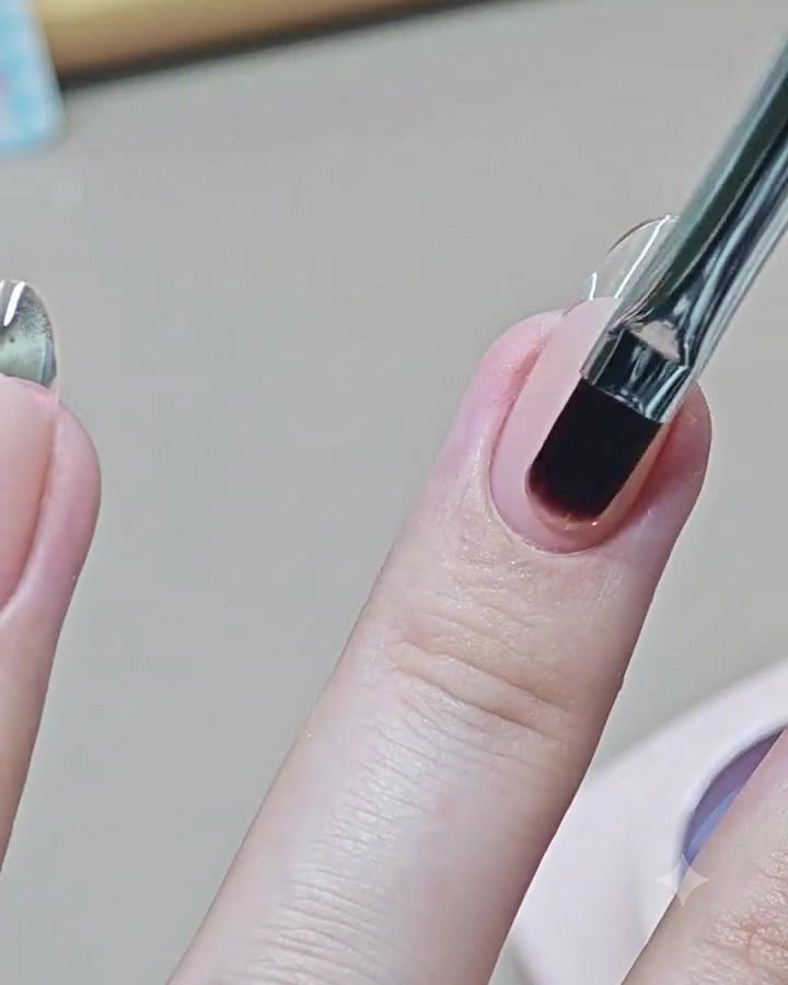 Un pincel de arte en uñas aplicando una capa superior transparente y brillante sobre una uña de manicura francesa terminada.