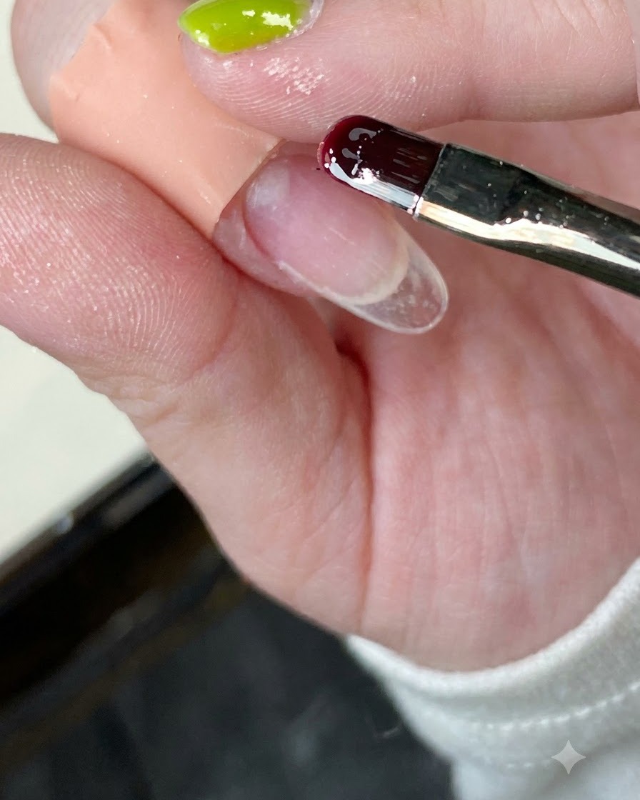 Primer plano de un pincel aplicando base transparente sobre un tip de uña.