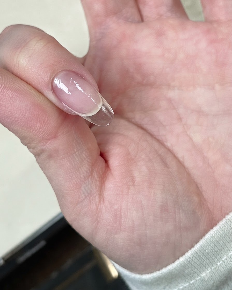 Una mano sosteniendo un tip de uña transparente bajo una mini lámpara LED.
