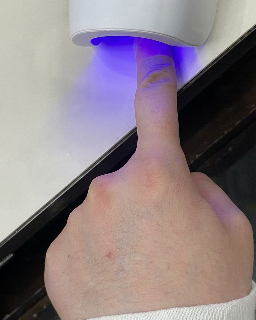 Un dedo colocado bajo una mini lámpara LED UV curando la capa de gel.