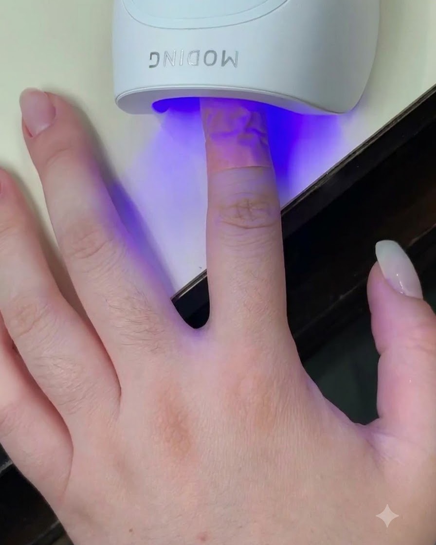 Un dedo dentro de una mini lámpara blanca de curado UV LED con luz azul brillando sobre la uña.