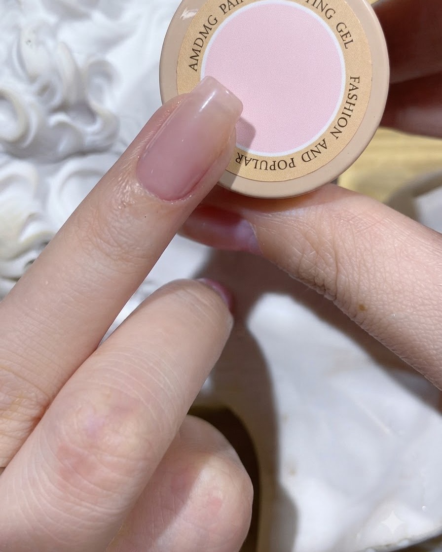 Una pequeña gota de gel rosa para patting colocada justo en el medio de una uña con capa base nude.
