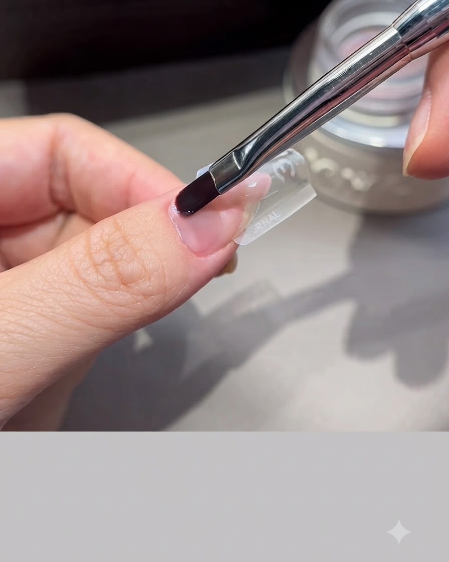 Una brocha profesional para uñas alisando el gel de extensión sobre un molde transparente posicionado en un dedo.