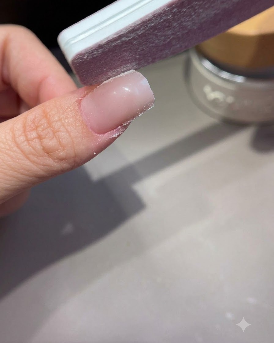 Una lima de mano dando forma y alisando los laterales de una uña extendida de acrílico o gel.