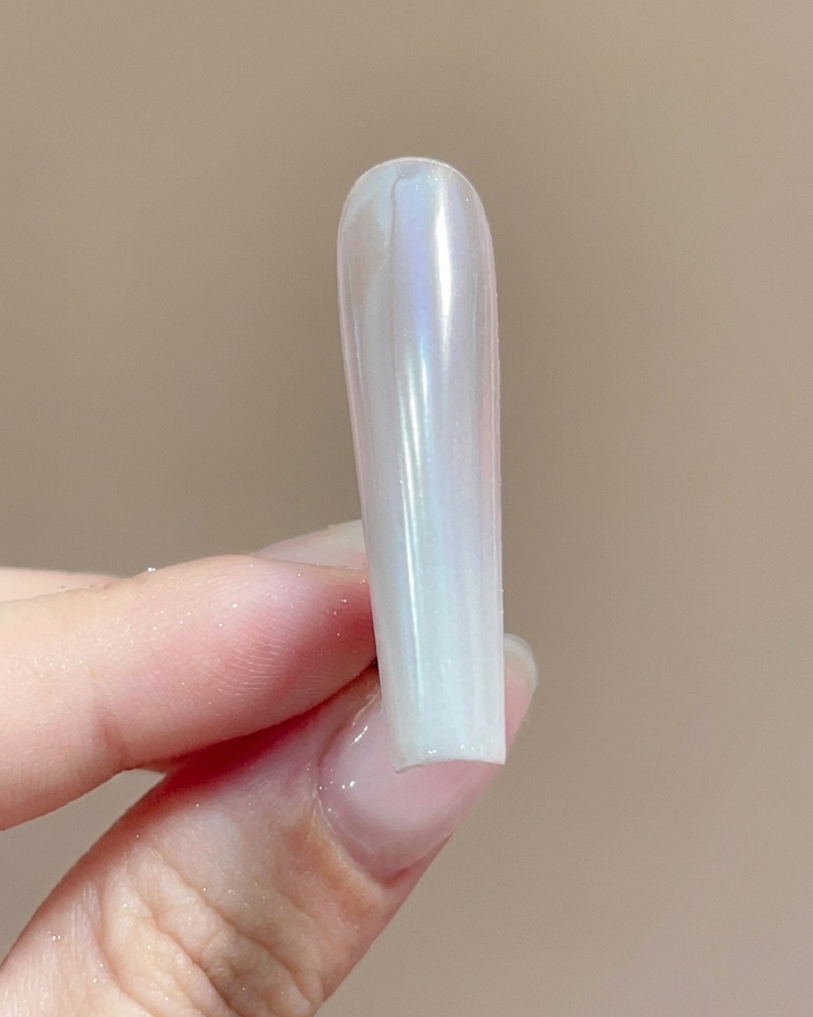 Un pincel aplicando un top coat transparente sobre una uña recubierta con polvo cromo brillante.