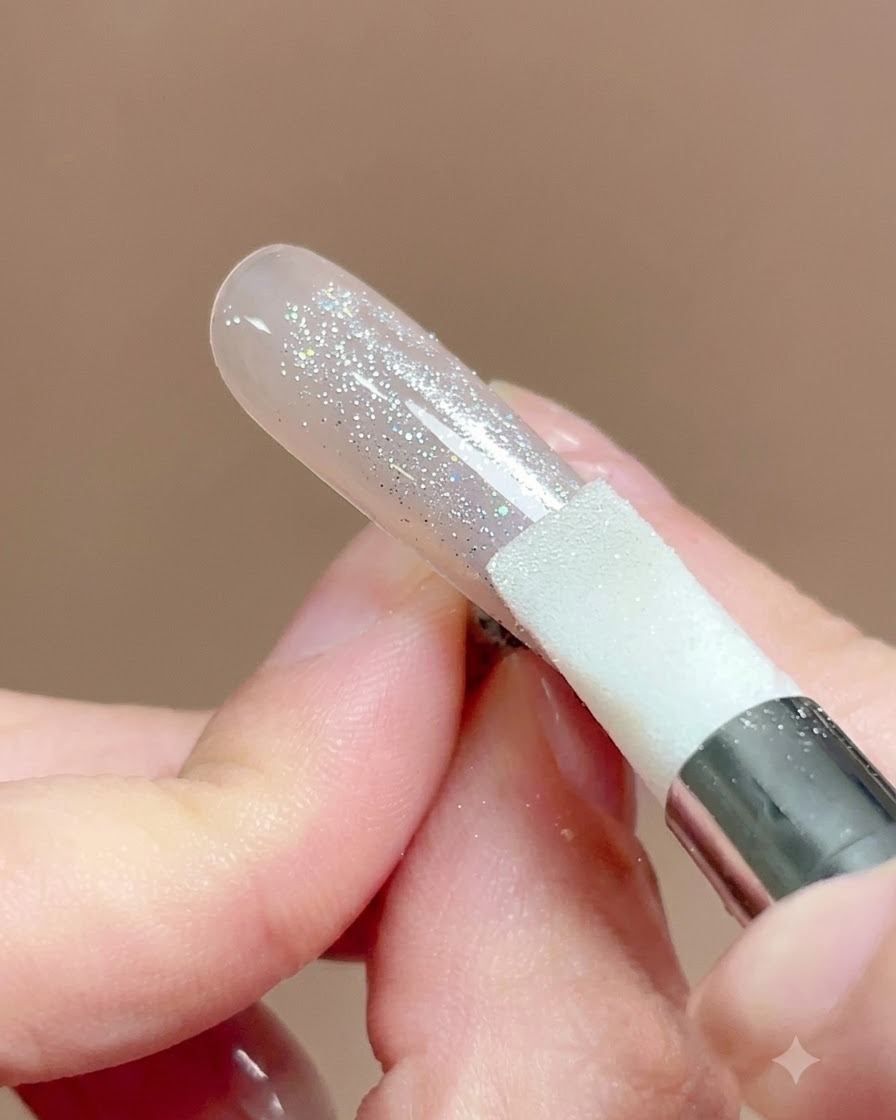 Un lápiz de silicona siendo presionado y frotado a través de la superficie de una uña cubierta con polvo cromo.