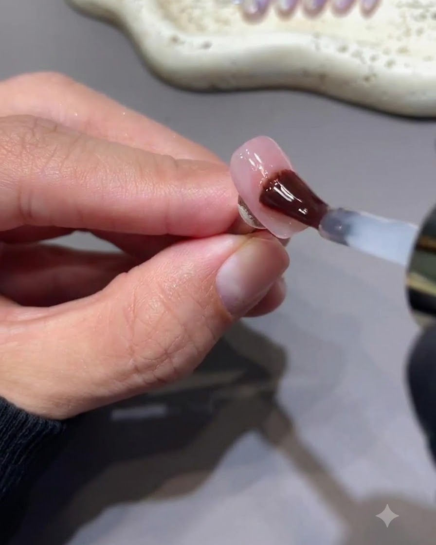 Un pincel aplicando una capa superior de gel brillante sin residuos sobre una uña con arte de estrellas rosa berry.