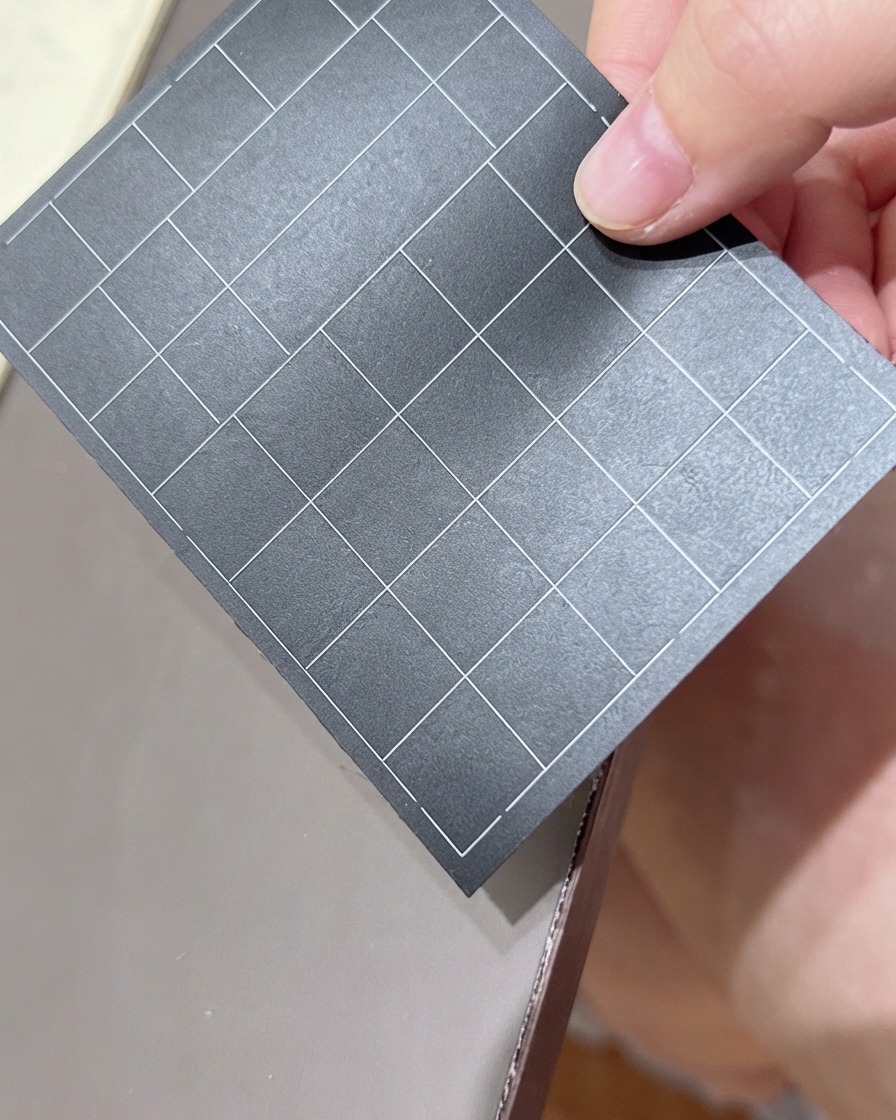 Una mano sosteniendo una hoja negra de pegatinas de uñas con cuadrícula, seleccionando una pegatina.