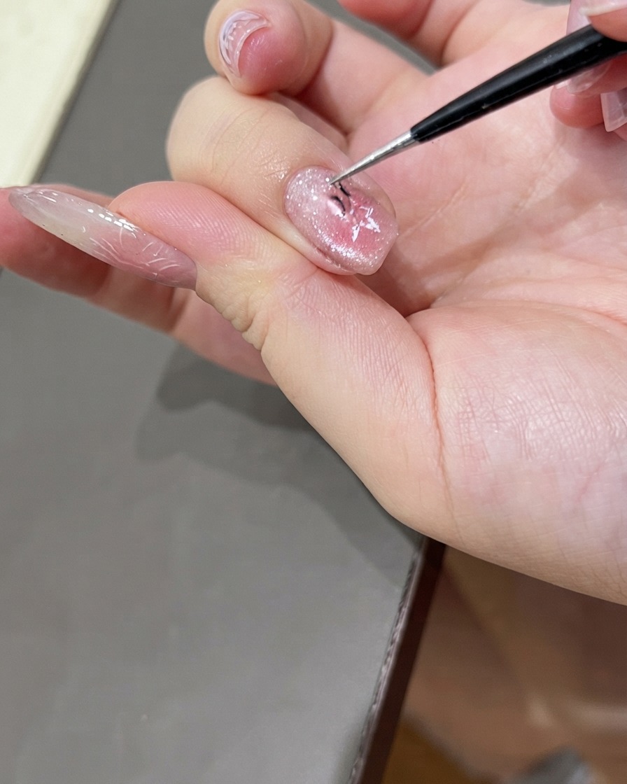 Un par de pinzas finas retirando delicadamente una pegatina de uñas en forma de estrella de una uña con manicura de gel ojo de gato brillante.