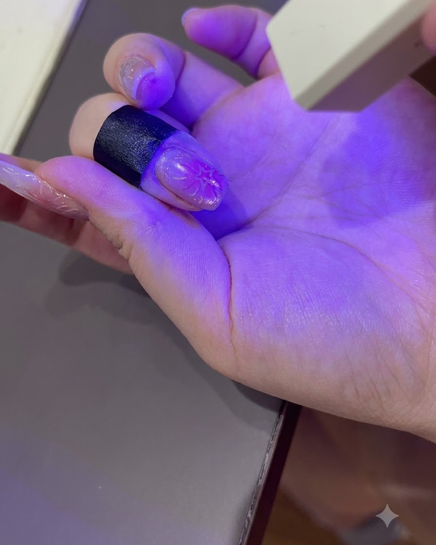 Una mano con manicura curando bajo la luz púrpura de una lámpara de uñas UV/LED portátil.