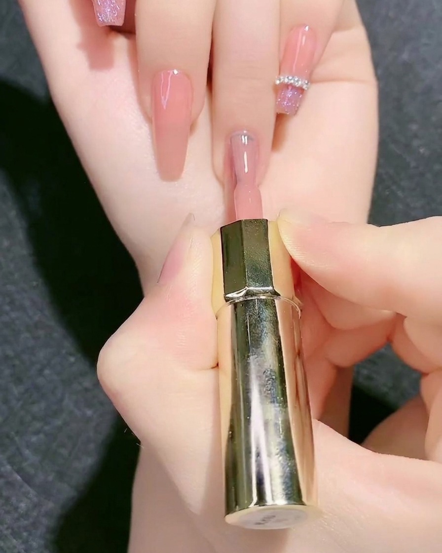 Un pincel de esmalte aplicando color base de gel rosa nude sobre la uña.