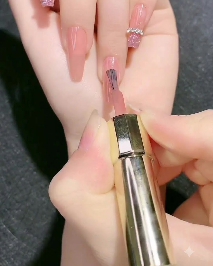 Un pincel aplicando una segunda capa de gel base rosa nude sobre la uña.