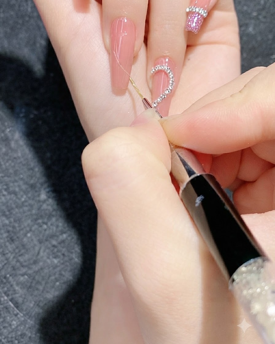 Una vista de cerca de una sesión detallada de nail art utilizando una herramienta fina para presionar tiras de cadena de strass en una uña con degradado.