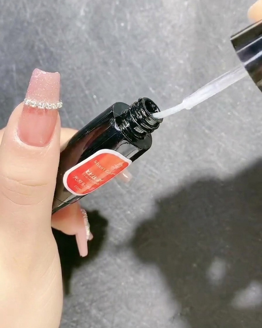 Un frasco de gel sellador transparente con un pincel aplicador utilizado para asegurar decoraciones de uñas.