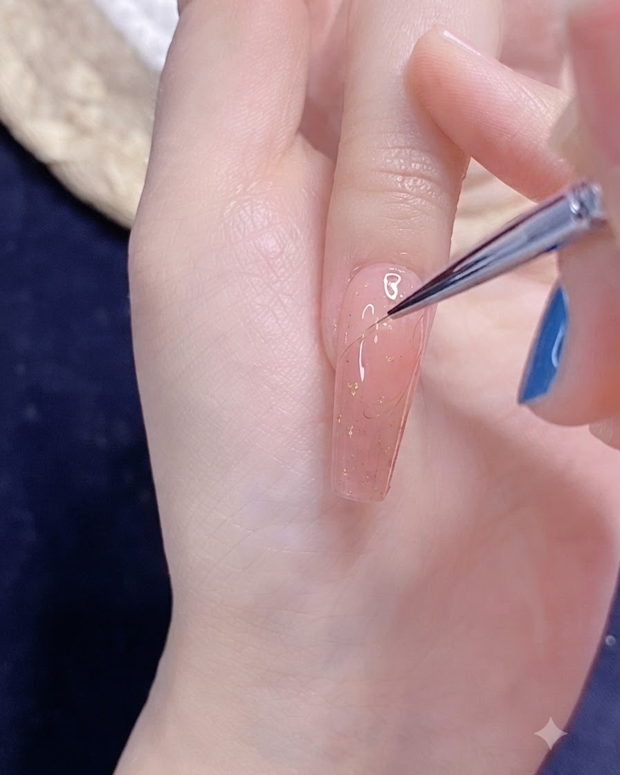 Un pincel fino de nail art dibujando un delicado contorno de medio corazón en gel sobre una uña pintada de rosa.