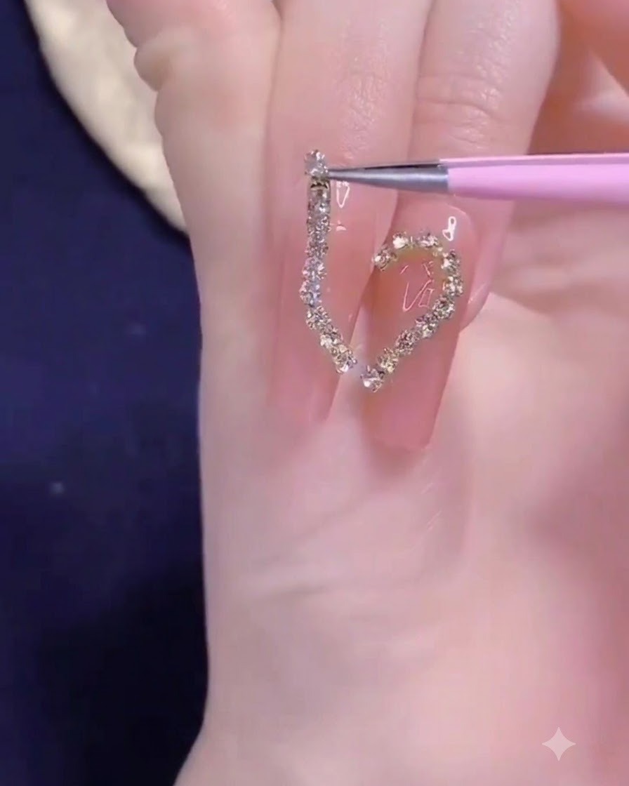 Un par de pinzas de precisión colocando una tira de cadena dorada sobre el diseño de medio corazón en la uña.