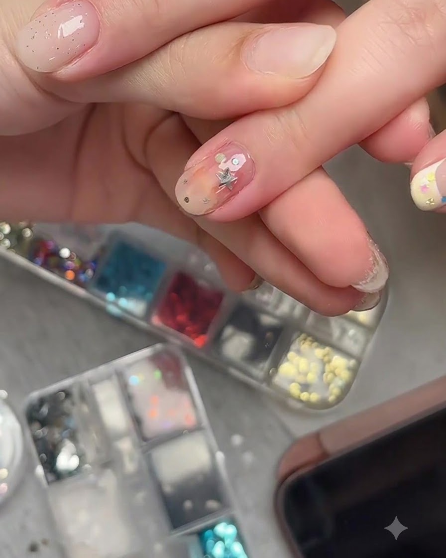 Ein Nail-Art-Pinsel trägt einen klaren Top Coat über eingebetteten Stern-Glitzerstücken auf einem fertigen Nagel auf.