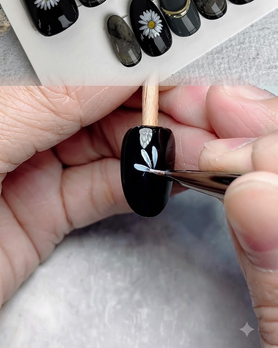 Un pincel de detalle fino añadiendo más pétalos blancos para completar la primera capa de la flor en una uña negra.
