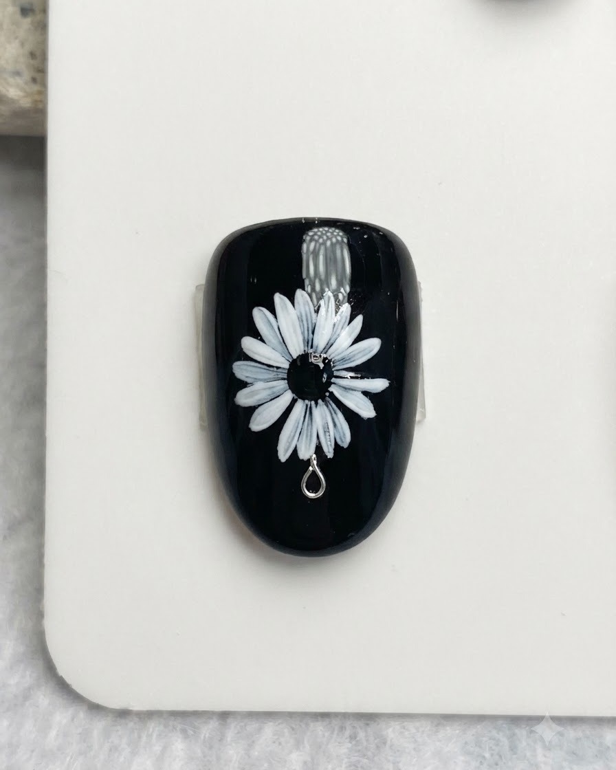 Primer plano de un pincel de uñas pintando delicados puntos blancos y amarillos sobre el centro negro de un diseño de margarita.