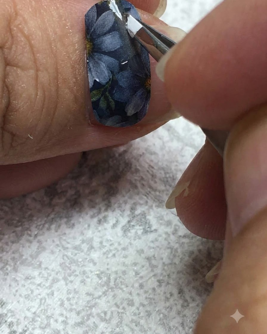 Un pincel delineador fino pintando cuidadosamente gel blanco en los pétalos de una margarita sobre una uña gris.