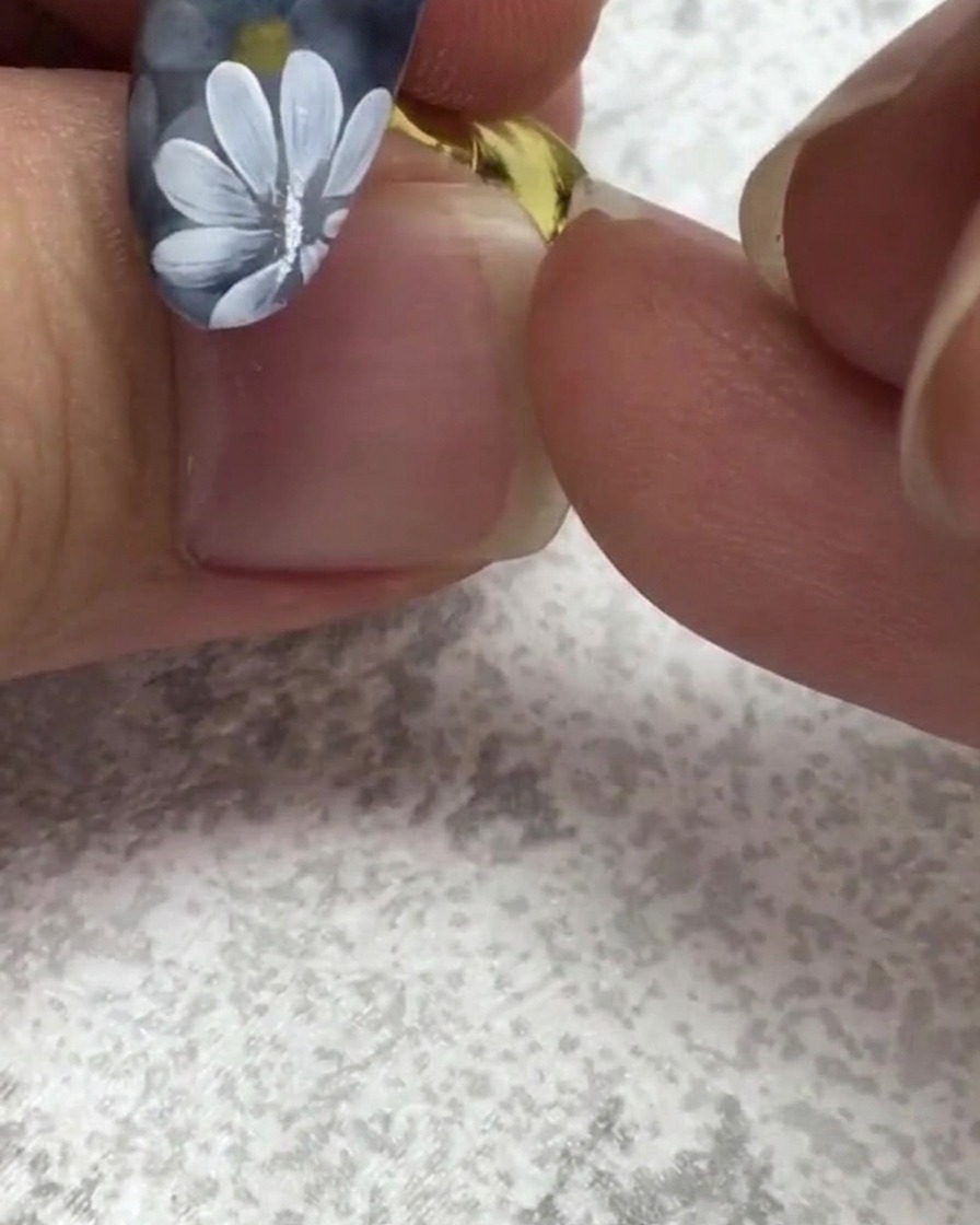 Un pincel para uñas plano tomando un pequeño punto de gel verde cerca de una uña con margaritas blancas.