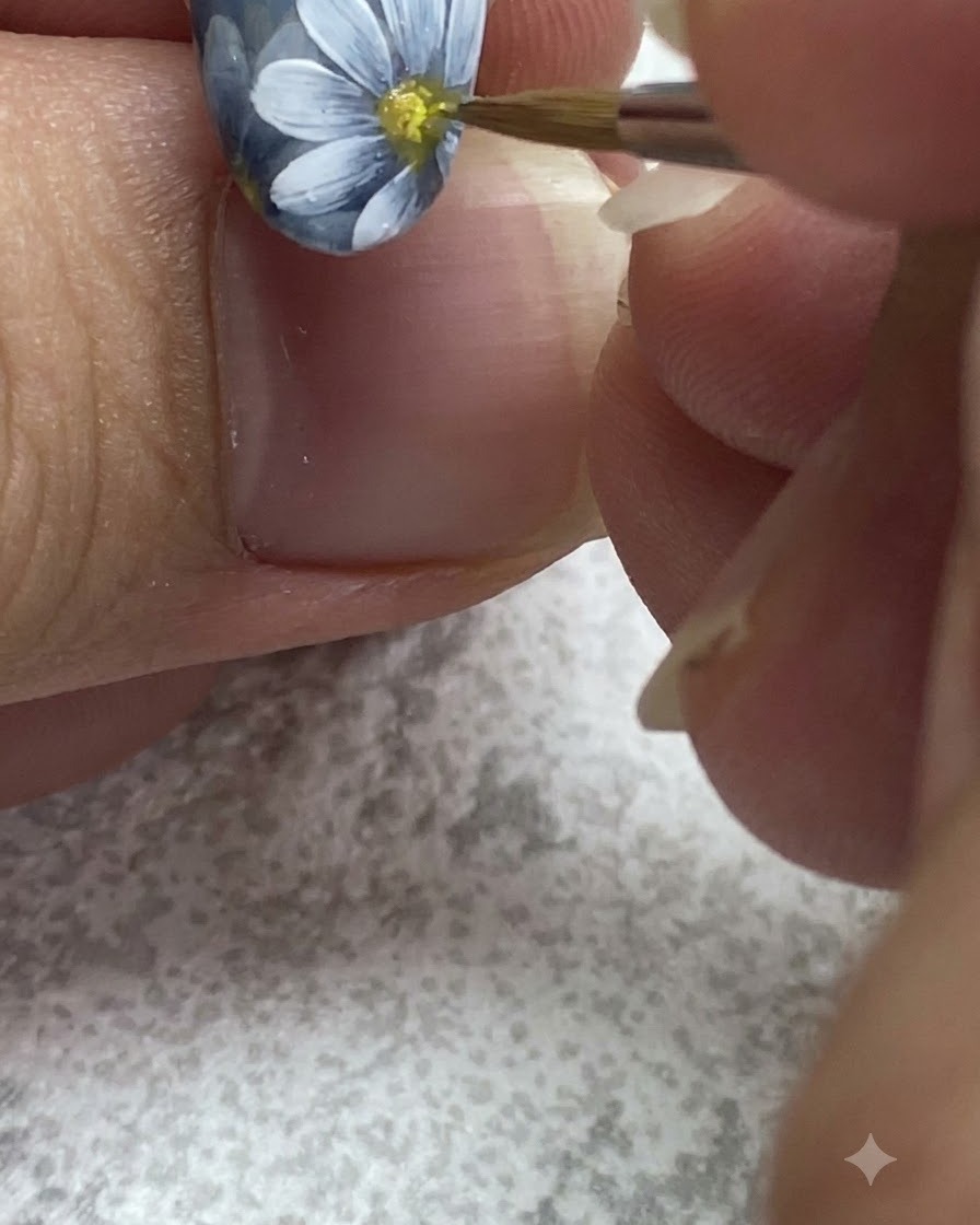 Un pincel fino aplicando gel amarillo en el centro de una margarita blanca pintada.