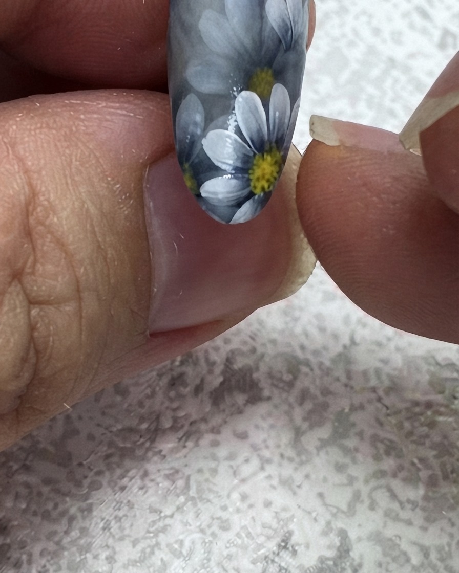 Un pincel delineador fino añadiendo una segunda hoja verde en la esquina superior de un diseño de uñas floral.