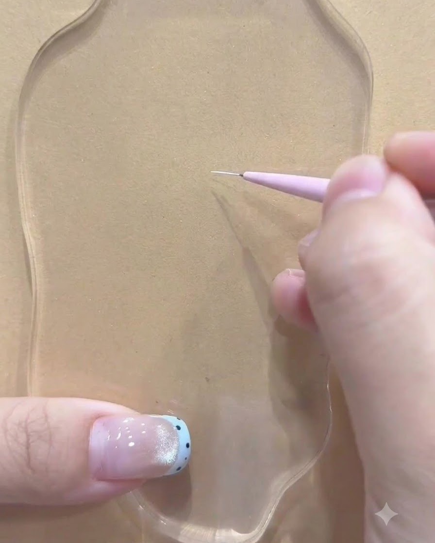 Un pincel delineador fino sostenido por una mano haciendo el primer trazo blanco sobre una paleta transparente.