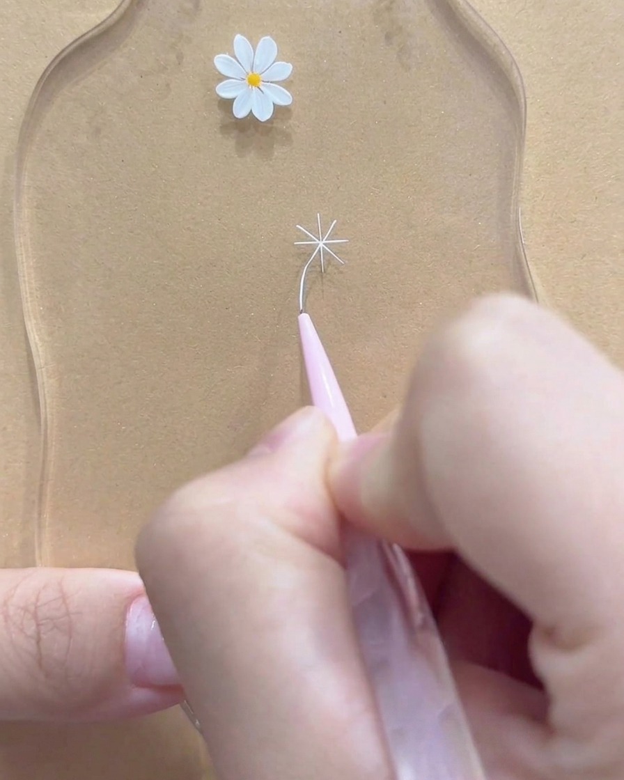 Un primer plano de un pincel delineador fino perfeccionando las puntas exteriores de una flor de margarita blanca.