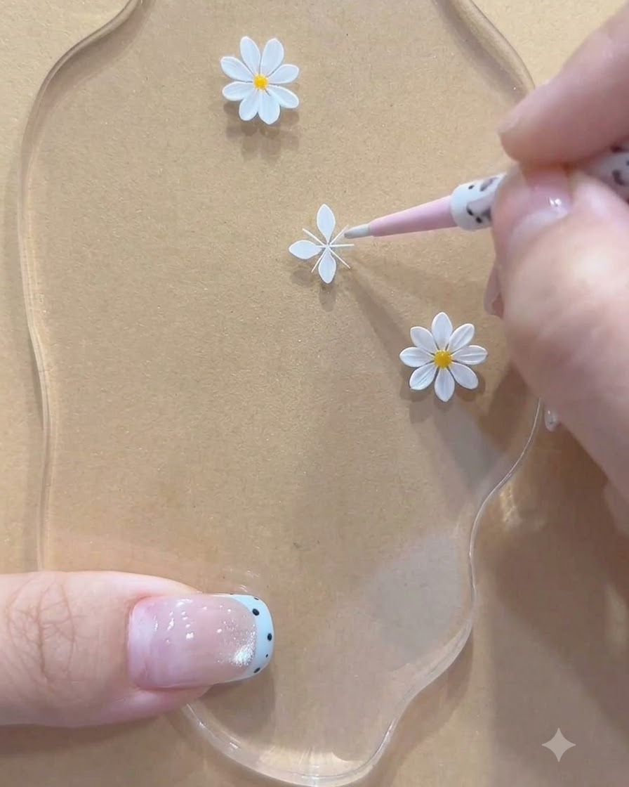 Una vista de primer plano de una herramienta rosa ajustando estructuras de pétalos blancos pintados para una margarita pequeña en una paleta acrílica.