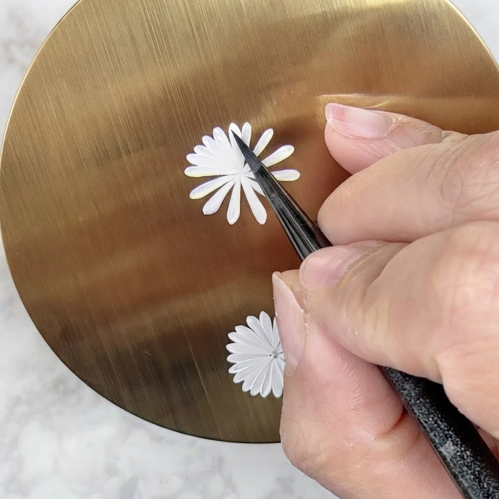 Un pincel de arte de uñas pintando cuidadosamente una segunda capa interna más pequeña de pétalos blancos en un diseño de margarita.