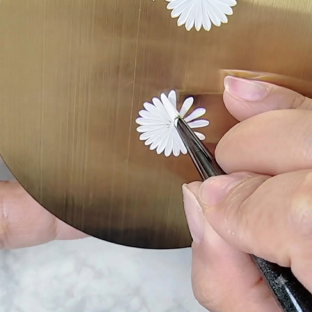 Una mano sosteniendo un pincel de arte de uñas en un ángulo ajustado para pintar detalles en un diseño de margarita sin girar la paleta.