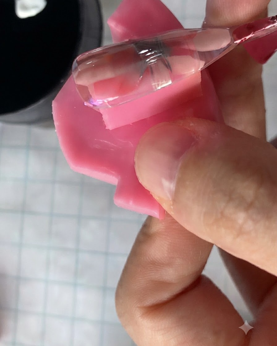 Un pequeño pincel de uñas aplicando un gel rosa translúcido sobre un diseño de flor de margarita curado en una uña.