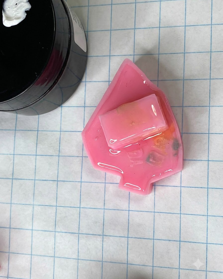 Un molde de uña rosa mate curado descansando sobre una alfombrilla de manualidades de cuadrícula junto a un tarro de gel.
