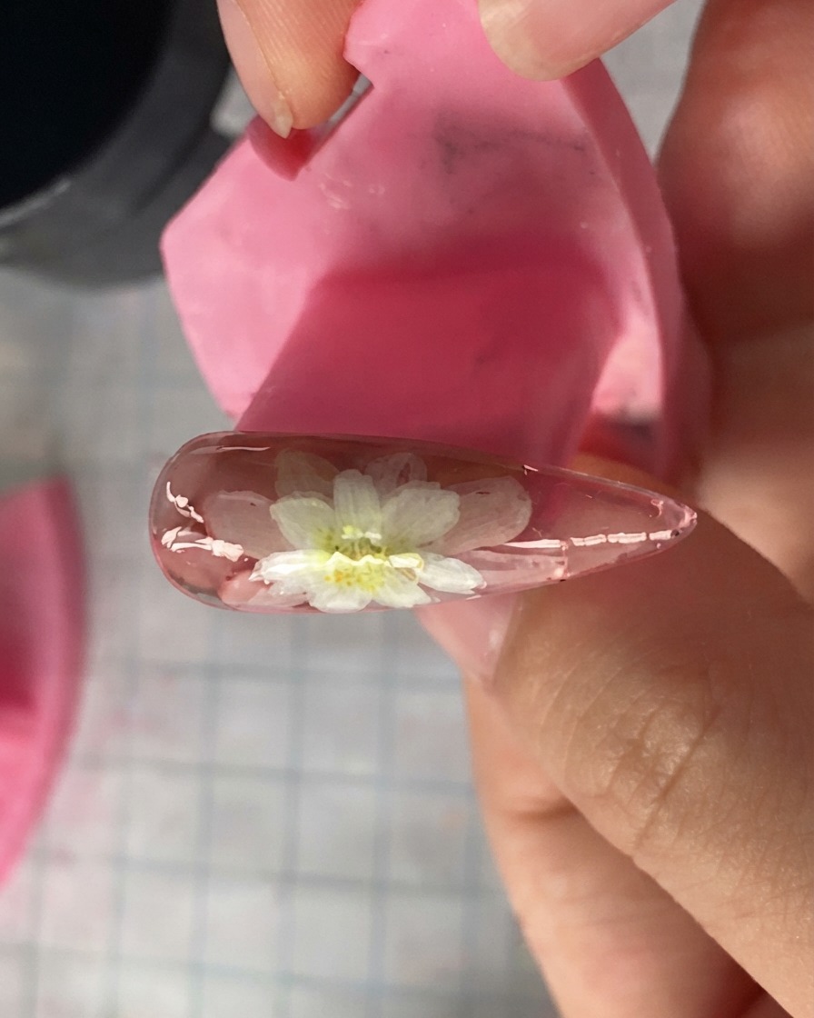 Una vista de cerca de un modelo de uña rosa que muestra pétalos de margarita blancos en capas pintados en la parte superior.
