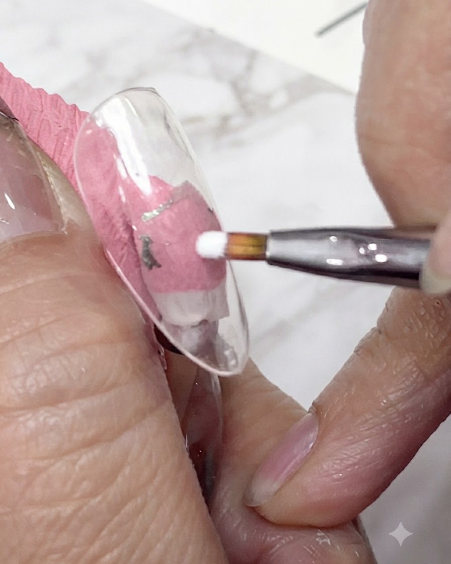 Una toma de cerca de un pincel delineador fino aplicando gel blanco para formar los primeros pétalos de una margarita en una punta de uña transparente.
