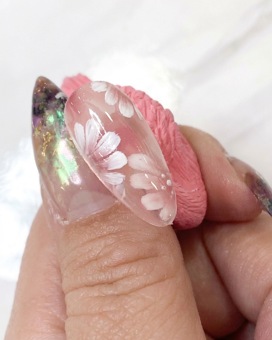 Una herramienta de punteado que aplica pequeños puntos de acento blancos alrededor del centro de la flor de un diseño detallado de arte de uñas.