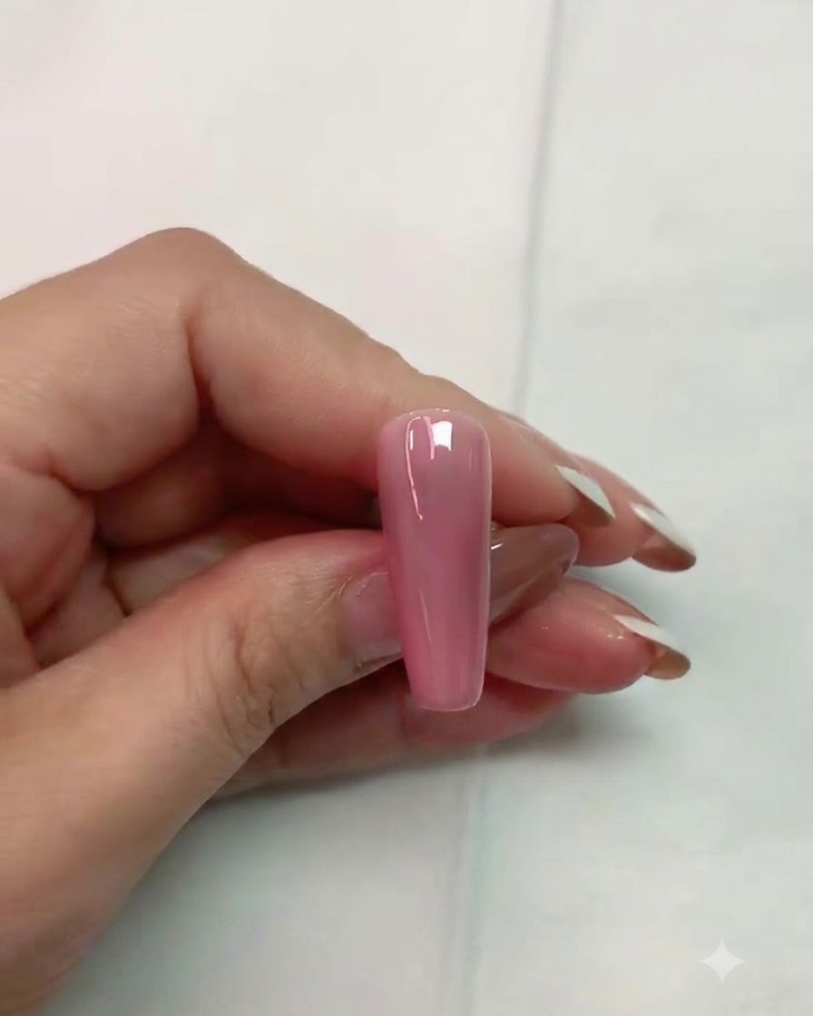 Un pincel aplicando una capa superior transparente mate sobre la superficie de una uña artificial rosa brillante.